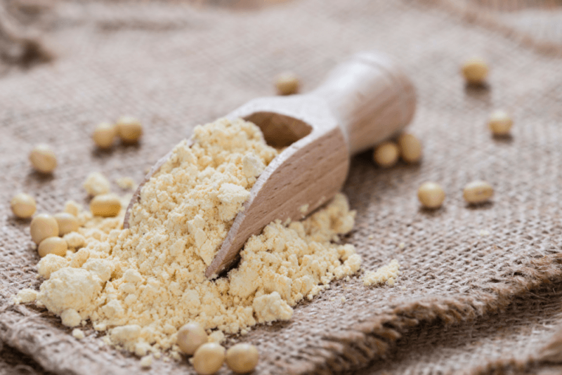 A cloth with some soybeans, a wooden scoop, and soybean flour.