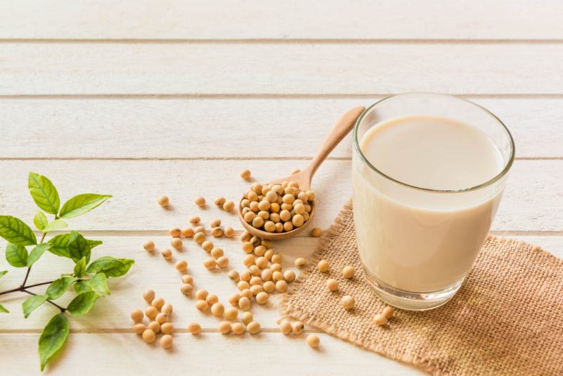 A glass of soy milk with soybeans on a light wooden table