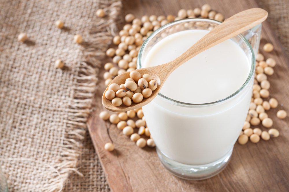 A glass of soy milk with a spoon of soybeans and various soybeans scattered around