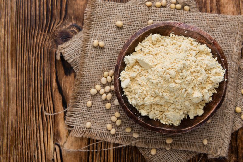 A bowl containing soy protein powder with soybeans scattered around