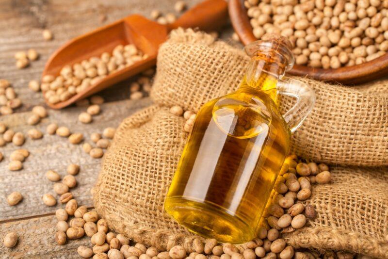 Sacks with soybeans and a bottle of soybean oil, including a bowl and a scoop of soybeans in the background