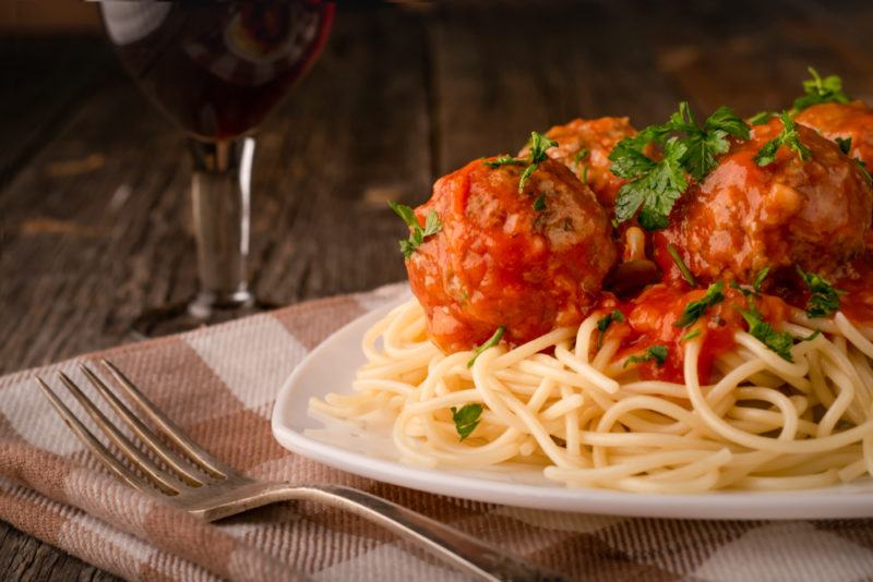 A white plate with pasta and meatballs next to a fork