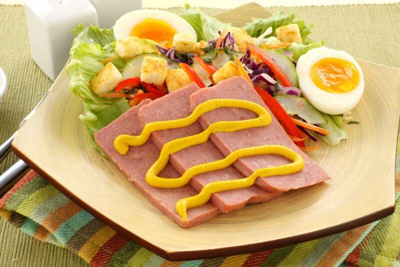 A plate with a salad, eggs, spam, and mustard