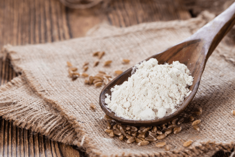 A wooden table with a cloth, spelt grains, and a wooden spoon of spelt flour