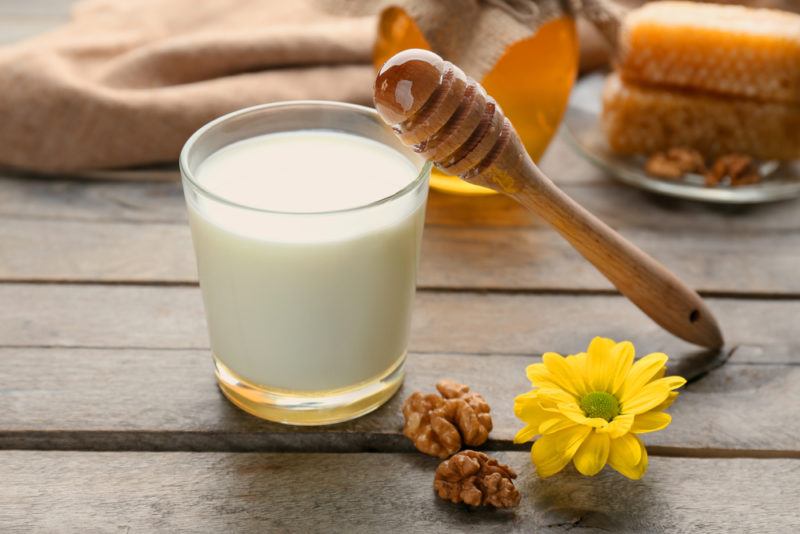 A glass of milk next to honey and some nuts