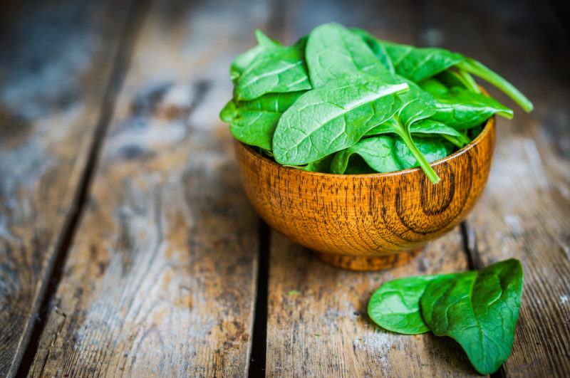 A wooden bowl containin spinach on a table