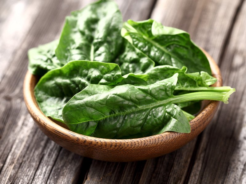 This photo shows a wooden bowl of spinach on a wooden table.