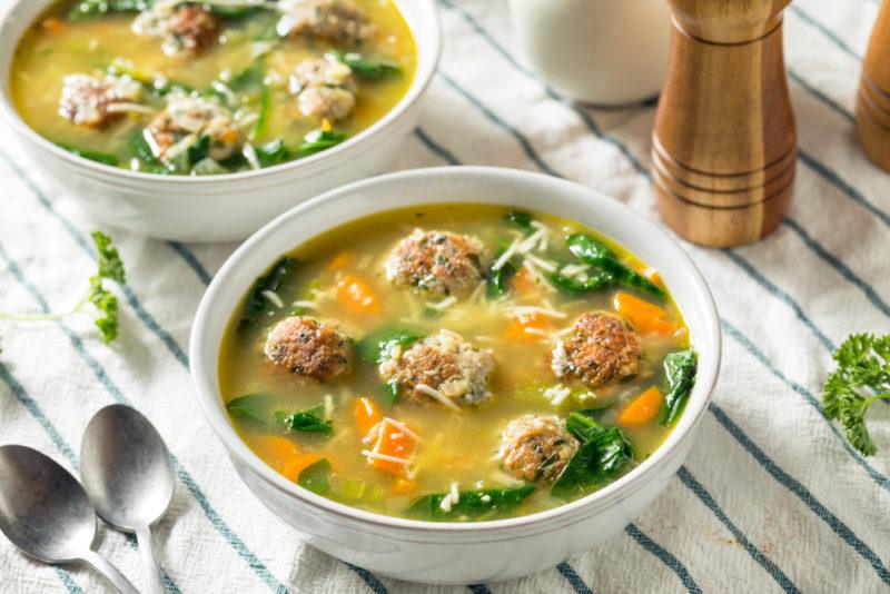 Spinach and meatball soup served in white bowls on a table cloth