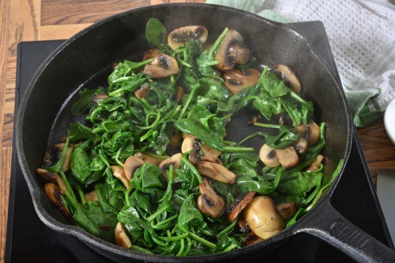 A black pan with spinach and mushrooms being sauteed