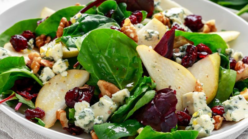 A salad containing spinach, pear, nuts and blue cheese