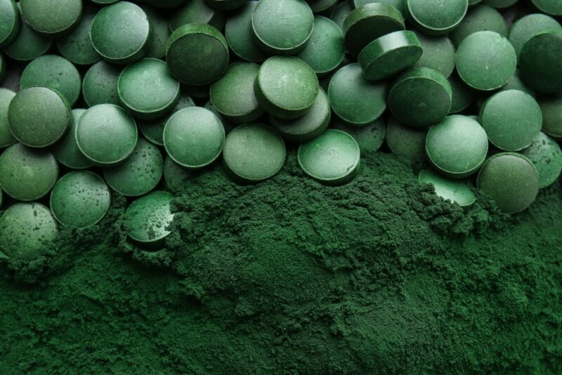 A selection of spirulina tablets, next to dark green spirulina powder