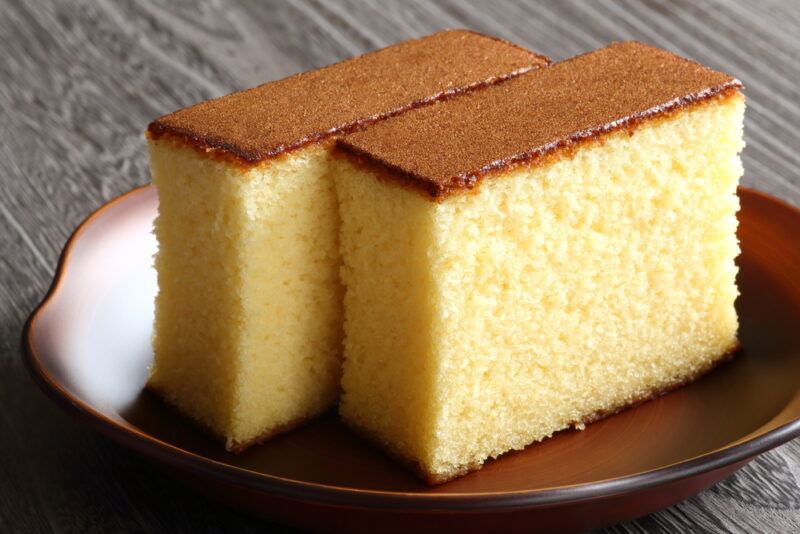 a couple of slices of sponge cake on a brown wooden dish resting on a dark wooden surface