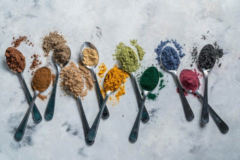 A table with a collection of small spoons, each containing a bright superfood powder