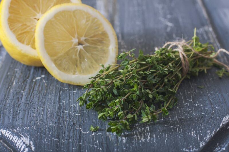 A gray table with a bundle of thyme, part of a lemon, and a lemon slice