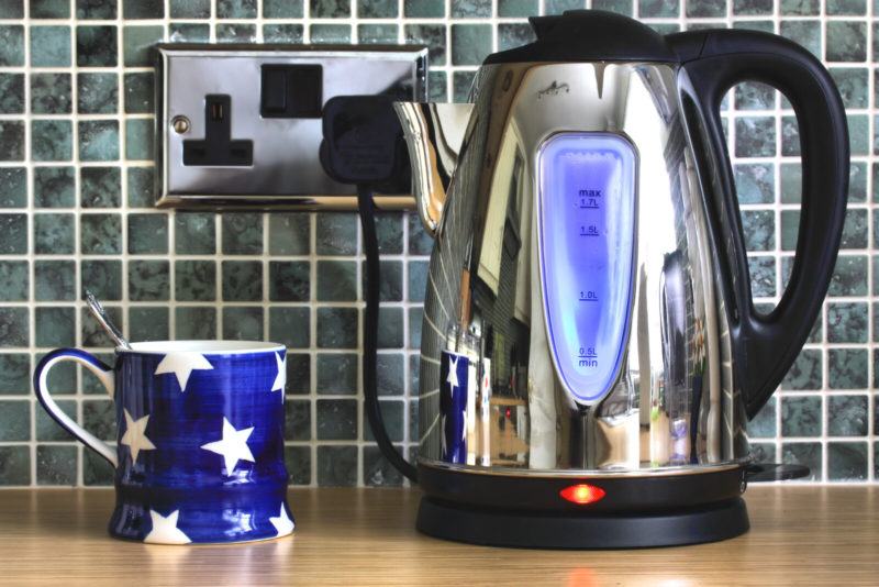 Stainless Steel Electric Kettle plugged into a outlet on a tile wall with a blue star themed mug