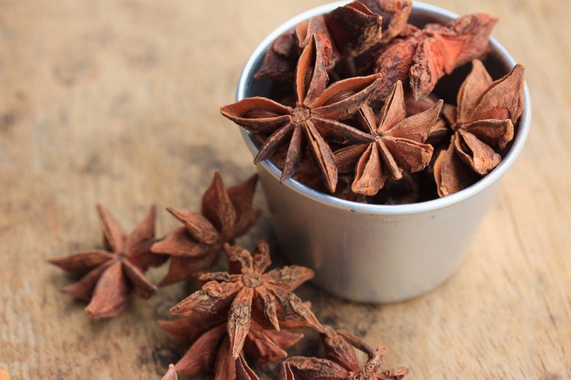 A small silver cup full of star anise with a few star anise beside it.