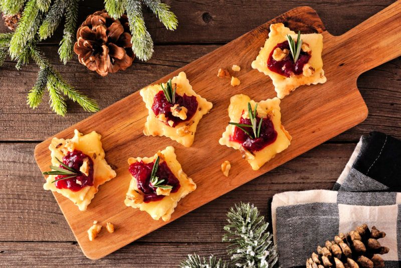 A wooden board with star shaped Christmass appetizers that use cranberry and brie as key ingredients