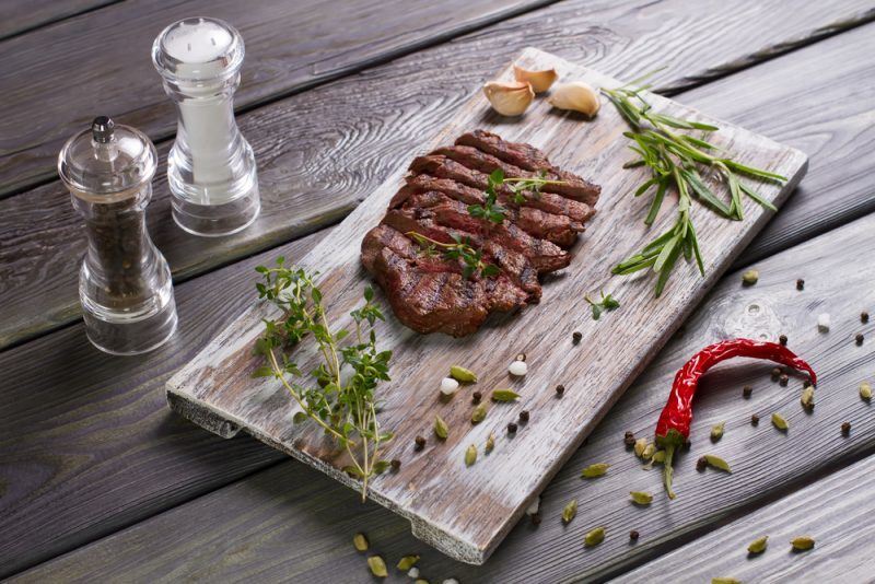 grilled steak cut into strips with herb garnishes, chilis, and salt and pepper shakers