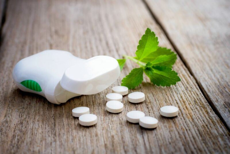 A wooden table with stevia tablets spilling out of a plastic container