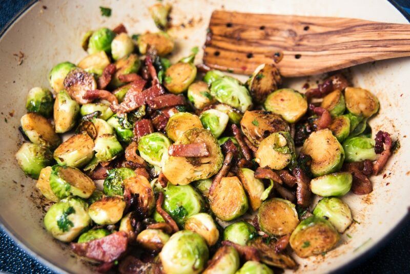 A wok filled with stir fried Brussels sprouts and a wooden spoon