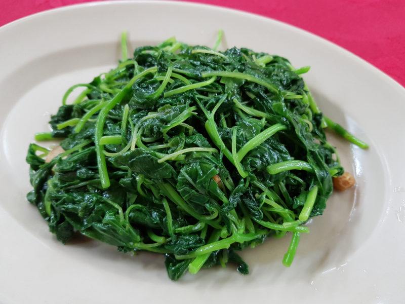 A white plate with spinach that has been stir fried with garlic