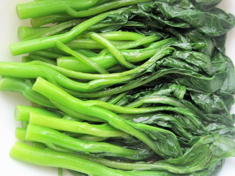 A selection of stir fried yu choy on white table, ready to be used as part of a meal