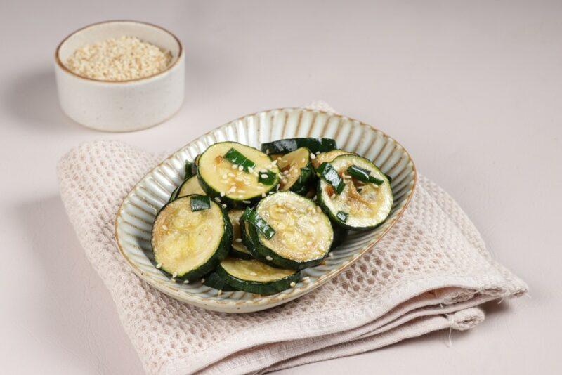 A white table with a cloth and a dish of stir fried zucchini