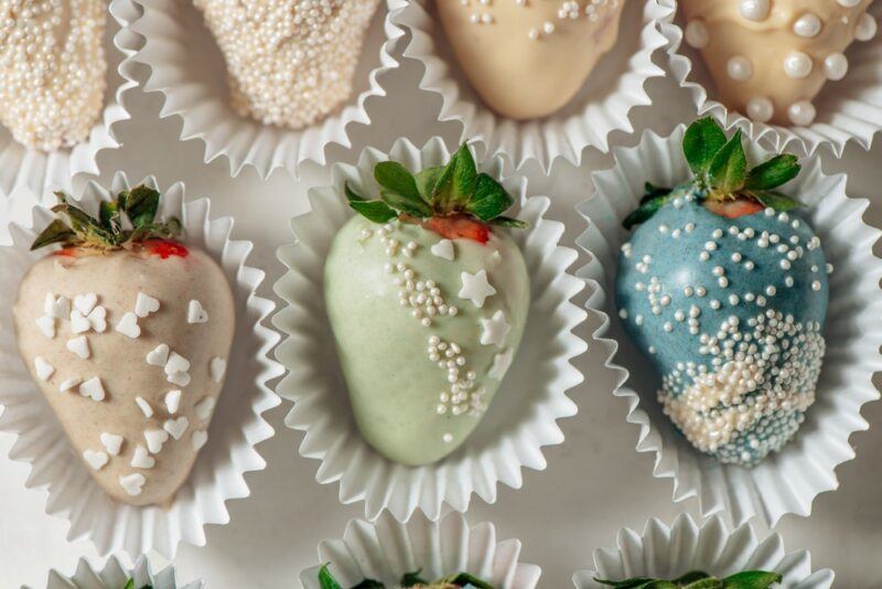 Cupcake liners each containing a strawberry that has been dipped in white chocolate and matcha, spirulina, or some other ingredient, then covered in sprinkles