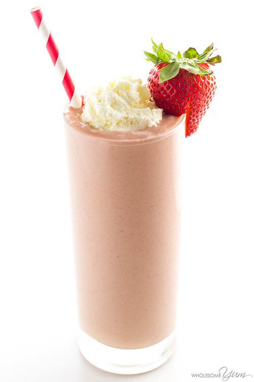 A light strawberry smoothie in a glass with cream and a strawberry.