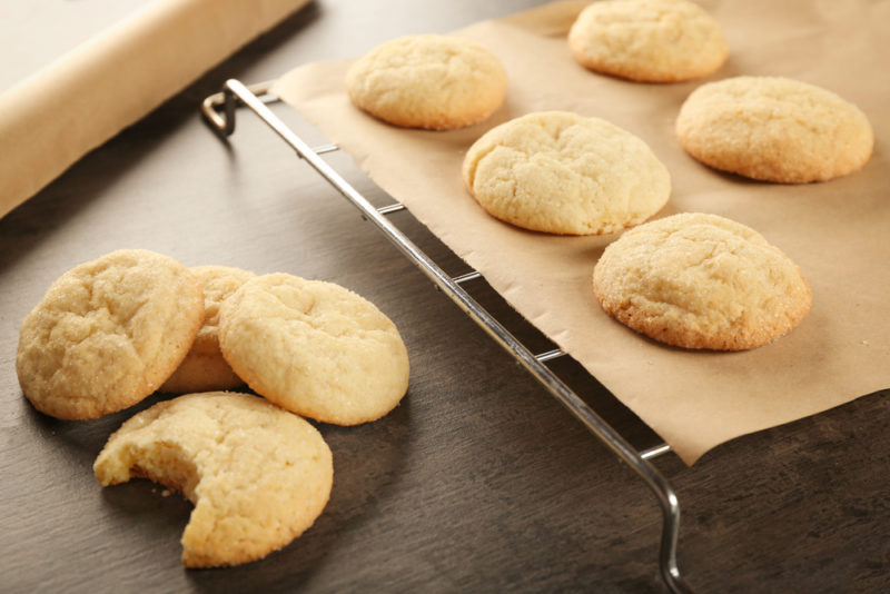 Sugar cookies on parchment paper on top of a baking tray, next to a small stack of sugar cookies