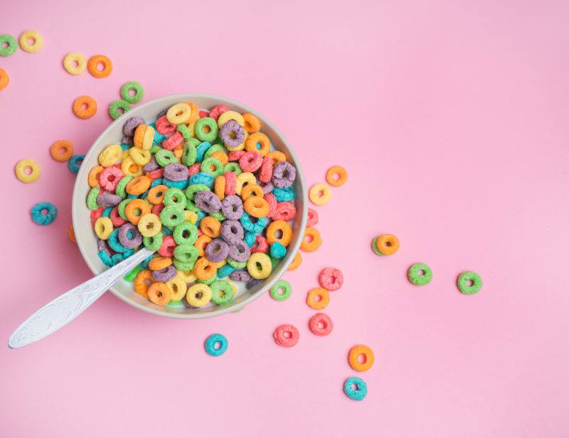 A white bowl of brightly colored cereal against a pink background