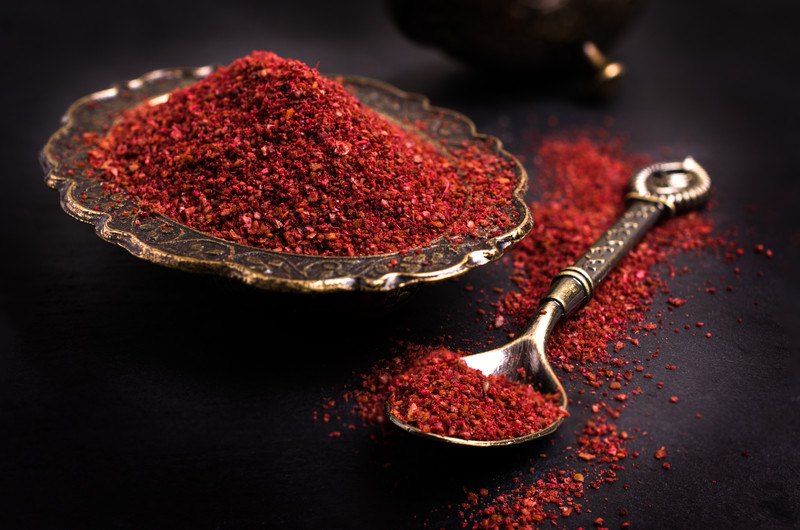 closeup image of a metal decorative plate and spoon full of sumac powder