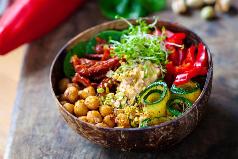 A brown bowl with sundried tomatoes, zucchini, and chickpeas