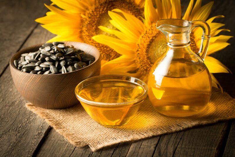 A table with sunflowers, a bowl of sunflower seeds, a bottle of sunflower oil and a dish of the oil