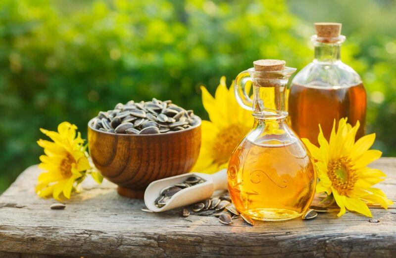 A wooden table outdoors with bottles of sunflower oil, a bowl of sunflower seeds, and some sunflowers