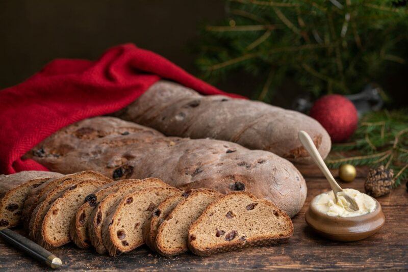 Two f3ull loaves of Swedish bread on a table, next to one that has been sliced, a red cloth and a spread