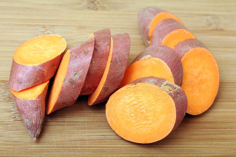 Several slices of orange sweet potato with a red skin rest on a wooden board.