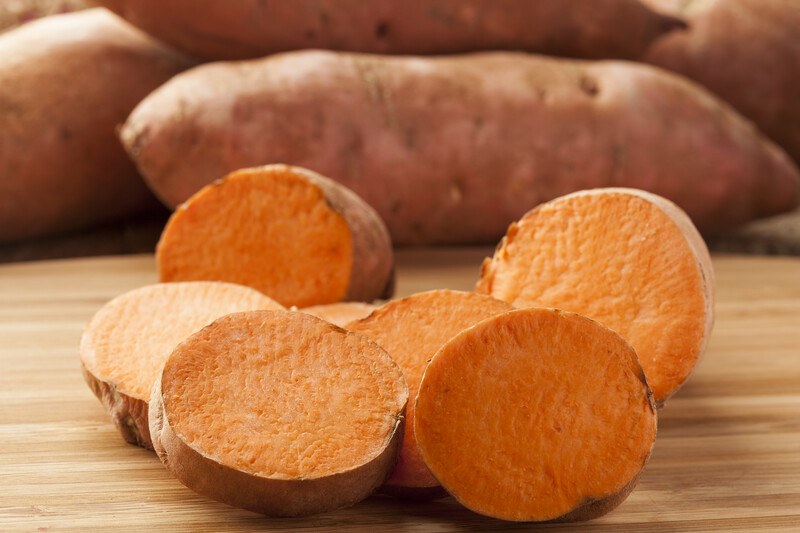 This photo shows several sweet potato slices on a wooden table near a pile of uncut sweet potatoes.