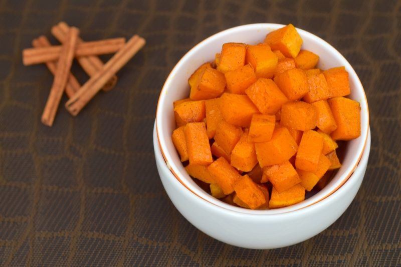 Cubed sweet potatoes in a white bowl next to cinnamon