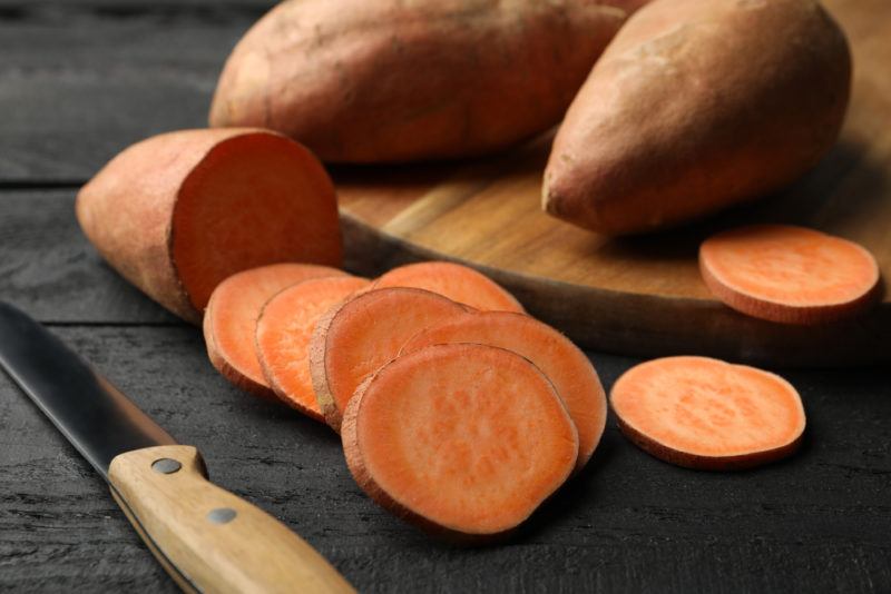 Two sweet potatoes on a board, with an extra one sliced