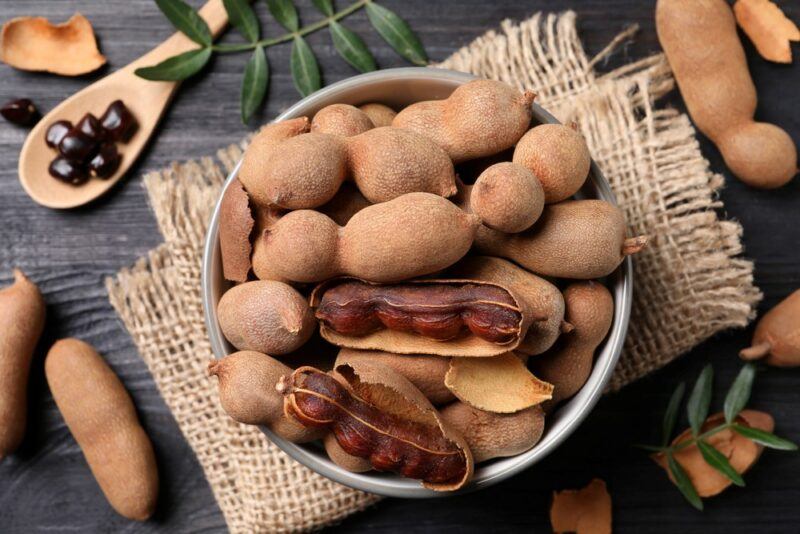 A piece of brown cloth with various tamarind fruits in a bowl