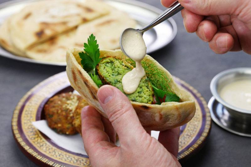 Someone putting falafel, sauce, and other ingredients into a pita pocket