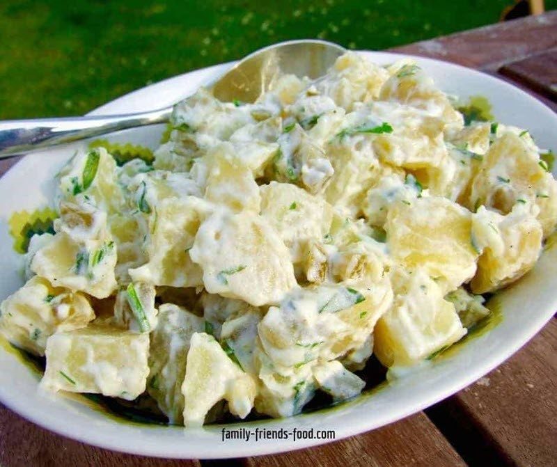 A white dish containing a tangy potato salad with fresh herbs