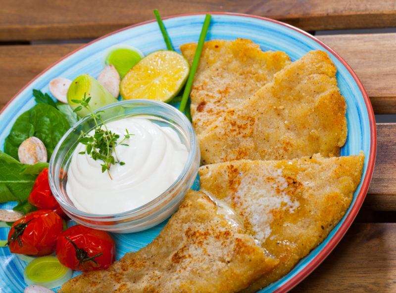 A blue plate with fried tattie scones, dips, and vegetables