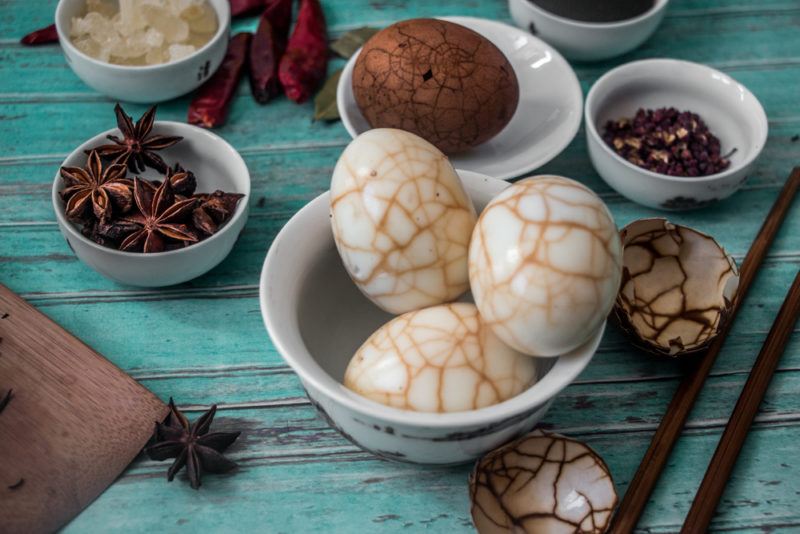 A small bowl with tea patterned tea eggs and various spices in the background