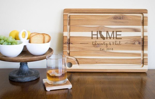 Teak-Cutting-Board | Food For Net A cutting board propped up against the wall, next to a stand and a whiskey glass.