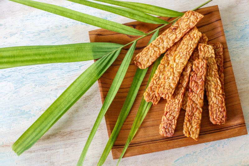 A wooden plate containing tempeh with leaves