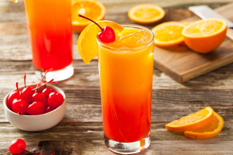 Two tequila sunrise cocktails on a table with slices of orange scattered around