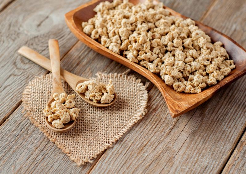 A brown plate with textured vegetable protein crumbles next to two spoons