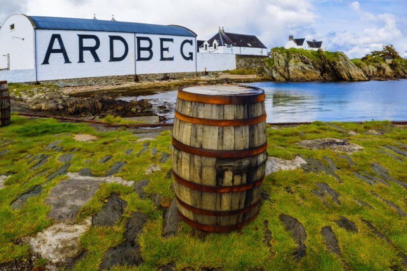 A barrel sitting on the bank with the Ardbeg distillery in the background